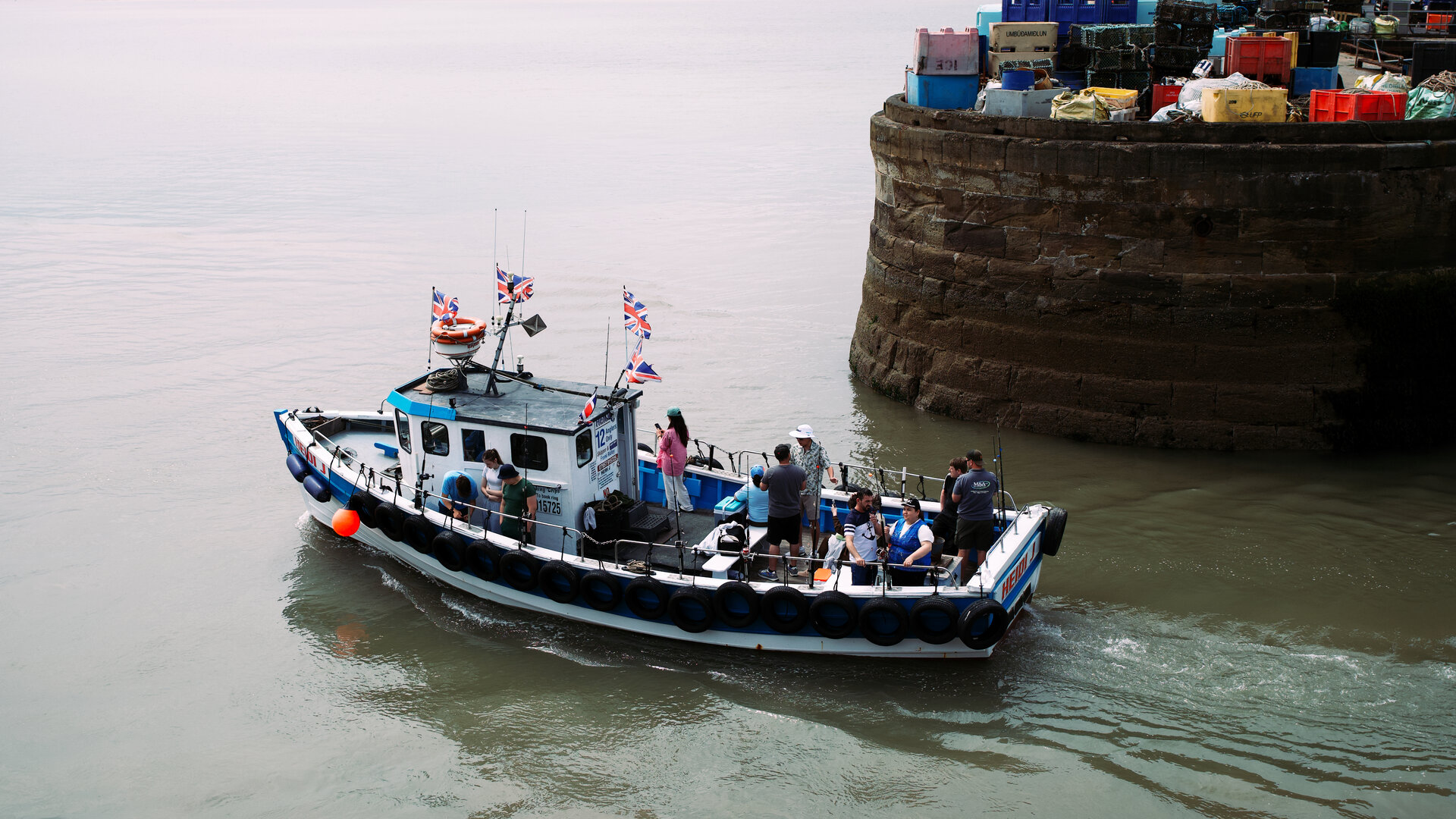 A fishing boat passing a stone harbour wall with passengers aboard