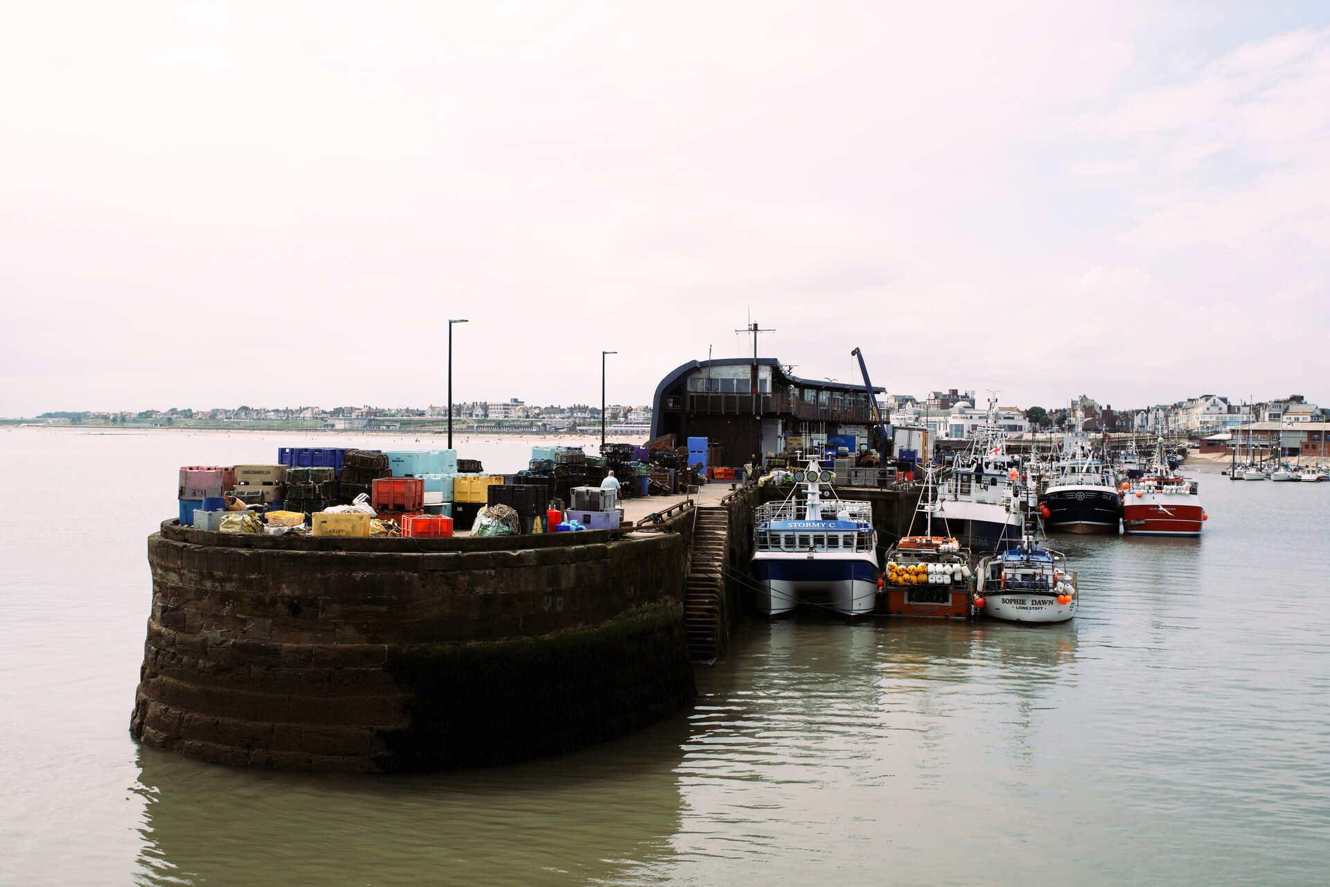 A stone harbour wall with crates stacked on top and fishing boats moored alongside